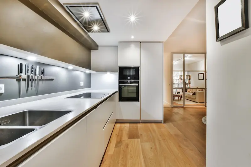 Cocina moderna con muebles blancos, encimera clara y suelo de madera